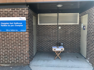 [Fieldhouse Doorway with a Small Table holding a box of Champlain Speaker Paper Copies]